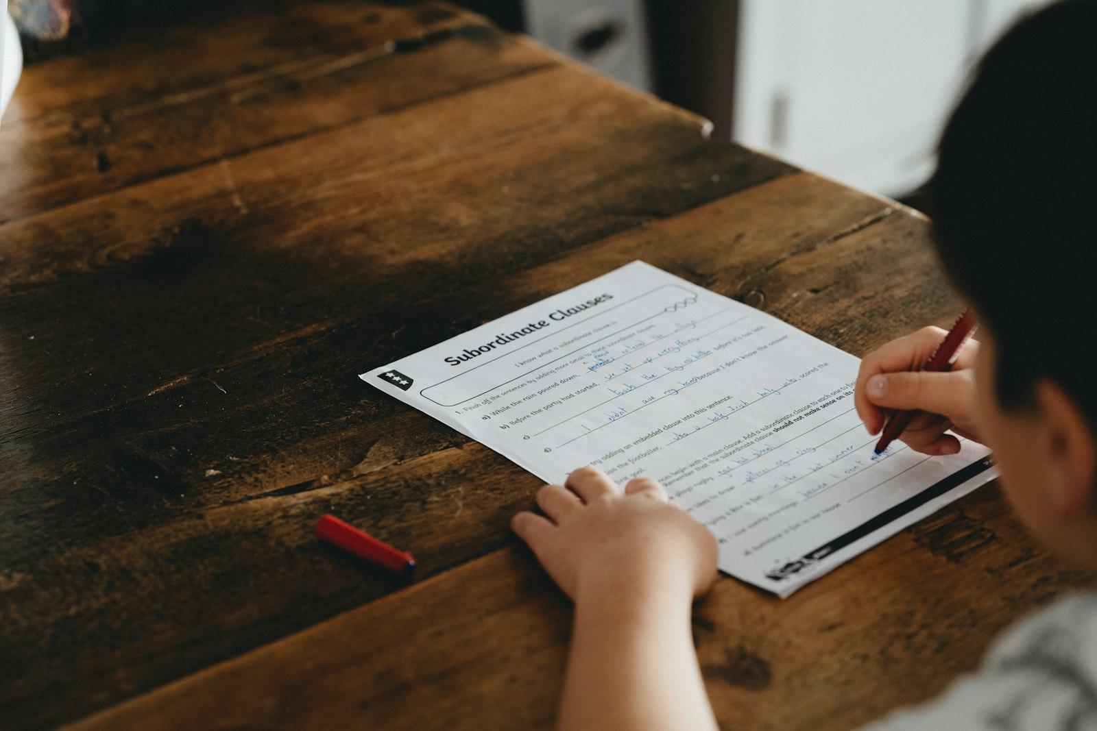 Person writing on white paper on brown wooden table