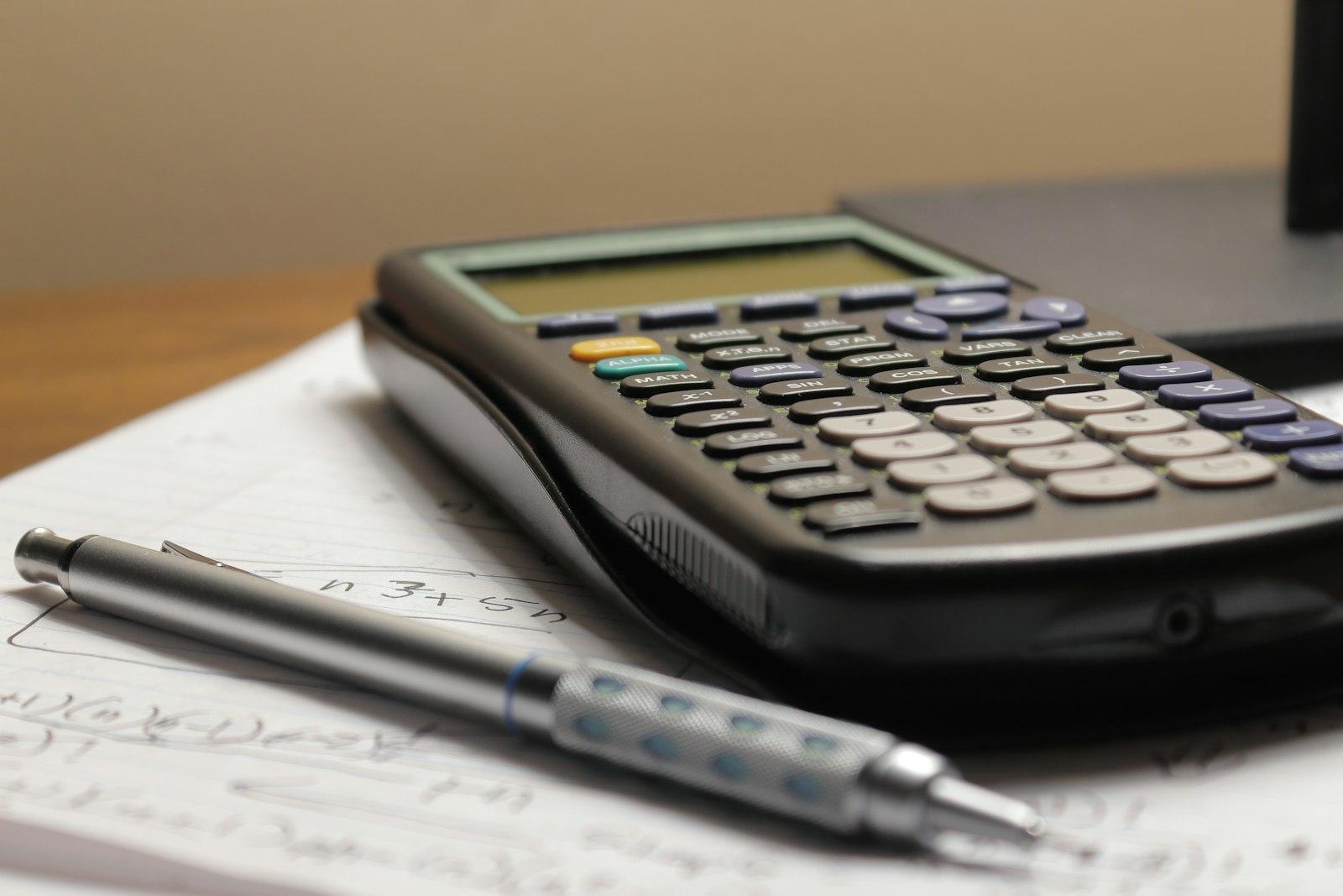 A calculator and a pen sitting on top of a piece of paper